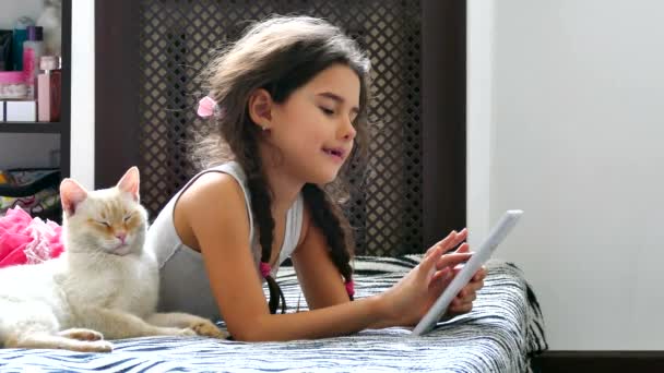 Girl teen playing tablet game internet sitting on bed next to the cat — Stock Video