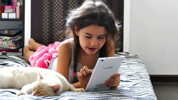 Girl teen playing tablet game internet sitting on bed next to cat — Stock Video