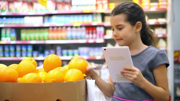 Menina adolescente com um tablet no supermercado para comprar laranja — Vídeo de Stock