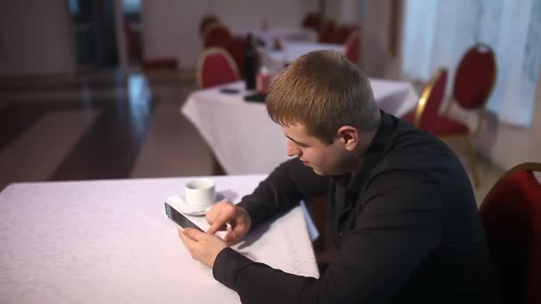 Человек держит смартфон просматривает интернет сидя в кафе — стоковое видео