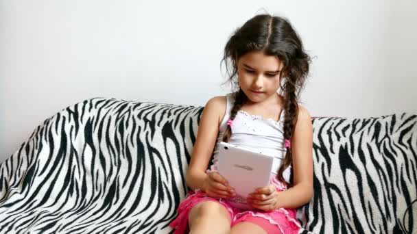 Дівчина-підліток грає в планшет, сидячи на ліжку — стокове відео
