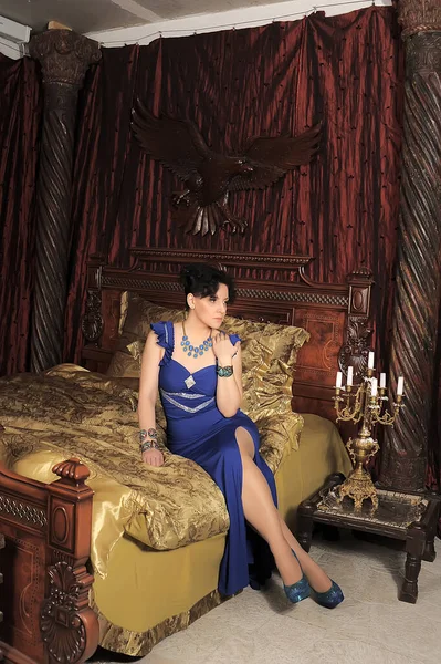 ブルネット女性で青ドレスでベッドでヴィンテージインテリア — ストック写真