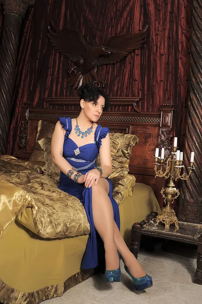 穿着蓝色衣服的黑发女士躺在旧式内饰的床上 — 图库照片