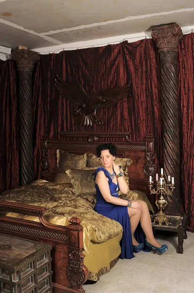 ブルネット女性で青ドレスでベッドでヴィンテージインテリア — ストック写真