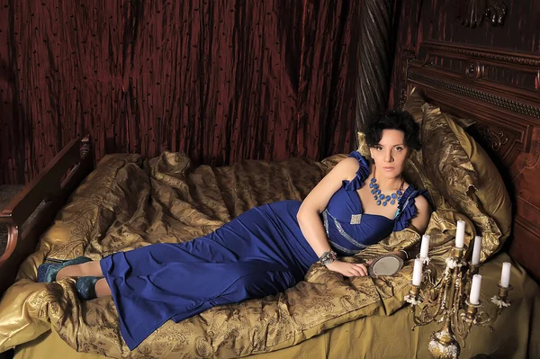 穿着蓝色衣服的黑发女士躺在旧式内饰的床上 — 图库照片