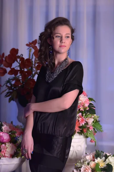 Chica en un vestido negro junto a un jarrón con flores — Foto de Stock