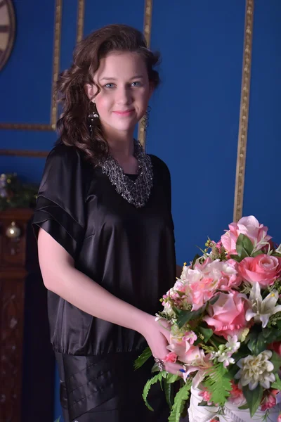 Chica en un vestido negro junto a un jarrón con flores — Foto de Stock