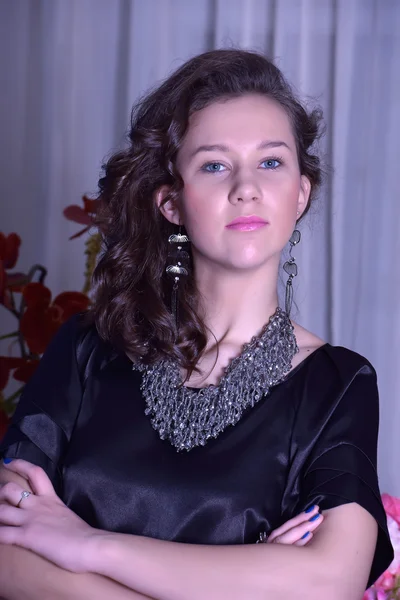 Chica en un vestido negro junto a un jarrón con flores — Foto de Stock