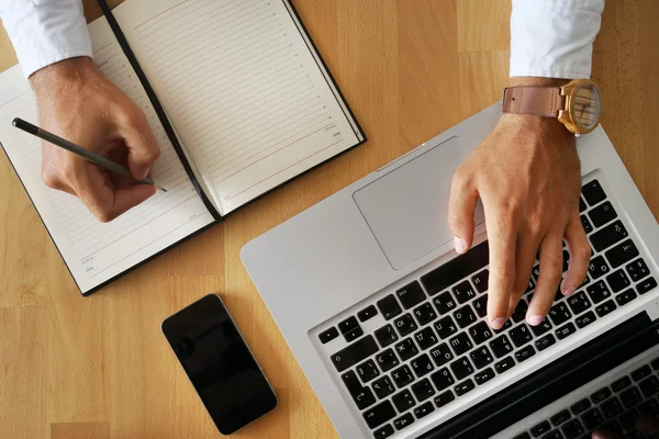 Ung mans hand ovanpå tangentbordet och med en penna i anteckningsboken skriver. — Stockfoto