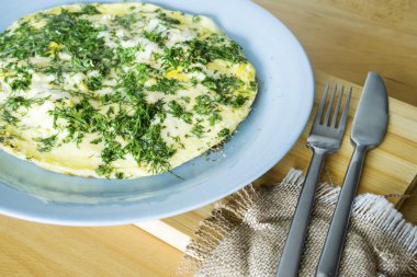 Ahşap bir masa üzerinde dereotu ile mavi bir plaka üzerinde omlet .