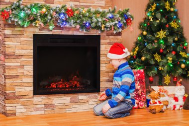 Şöminenin oturan Noel şapkalı çocuk 