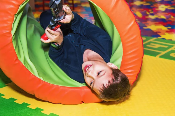 快乐的男孩很开心 他手里拿着玩具枪躺在地板上 — 图库照片