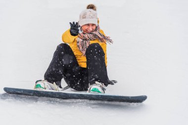Snowboard 'da bir dağın kenarında oturan neşeli genç kadın.