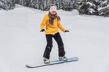 Genç, neşeli bir kadın tepeden aşağıya bir snowboard 'un üzerinde yuvarlanıyor.