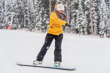 Genç, neşeli bir kadın tepeden aşağıya bir snowboard 'un üzerinde yuvarlanıyor.