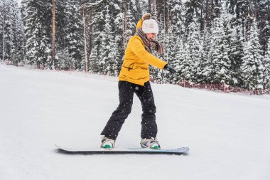Genç, neşeli bir kadın tepeden aşağıya bir snowboard 'un üzerinde yuvarlanıyor.