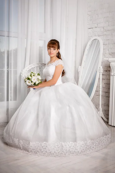 Bride with wedding bouquet sits in an armchair near window — Stock Photo, Image