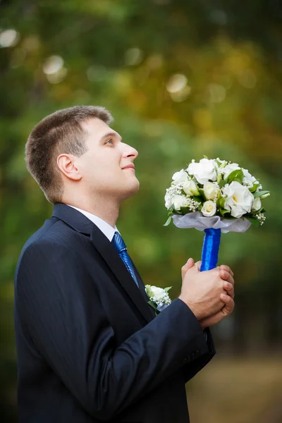 El novio sostiene un ramo de novia de boda en la mano y mira hacia arriba —  Fotos de Stock