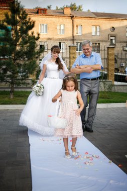 Baba ve gelin sunak için gidiyoruz ve kız onlardan önce gül yaprakları atıyor.