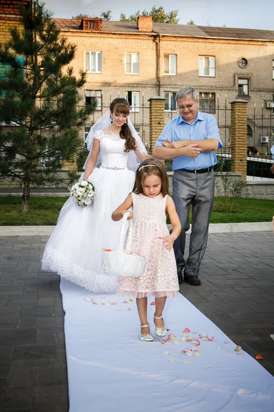Baba ve gelin sunak için gidiyoruz ve kız onlardan önce gül yaprakları atıyor.
