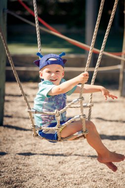 Mavi şapkalı yakışıklı bir çocuk salıncakta sallanıyor..