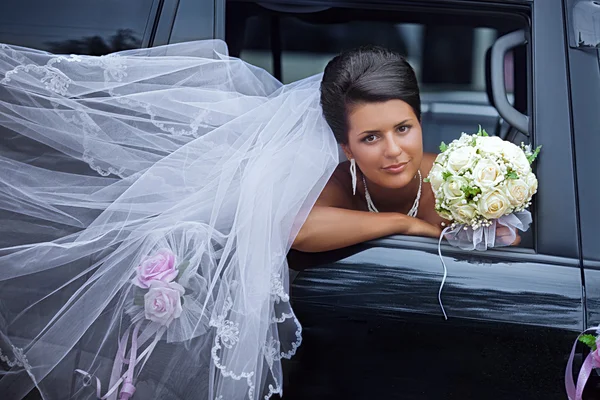 Braut mit dem flatternden Schleier blickt aus dem Autofenster — Stockfoto
