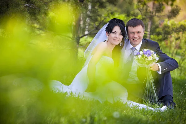 Bruid en bruidegom knuffelen en kijken in de ogen van een ander zittend op een groen gras — Stockfoto