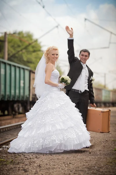 Ženich a nevěsta s kufrem na nádraží — Stock fotografie