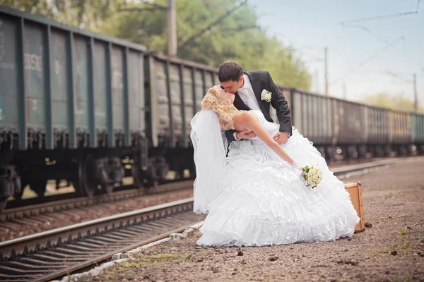 Ženich a nevěsta s kufrem na nádraží — Stock fotografie