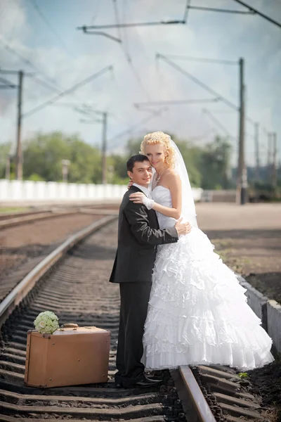 Ženich a nevěsta s kufrem na nádraží — Stock fotografie