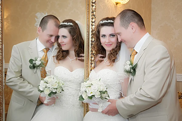 Groom and the bride stand near a mirror with a gold frame — Stock Photo, Image