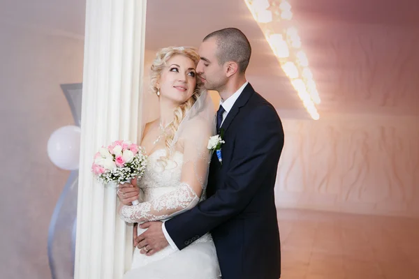 Novio y la novia de pie con un ramo de bodas cerca de una columna blanca — Foto de Stock