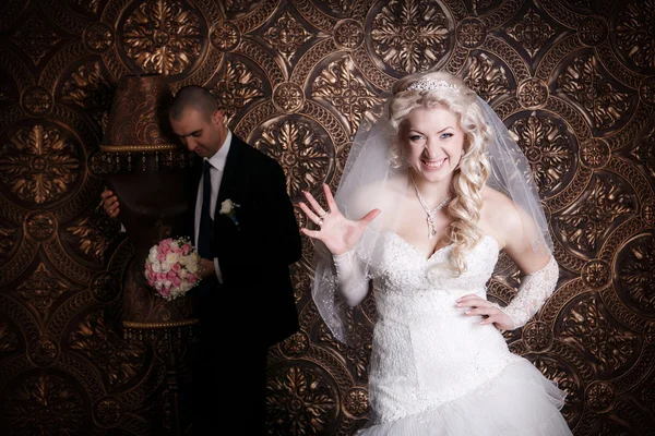 O noivo feliz e a noiva encantadora com um buquê de rosas no estúdio em um contexto marrom — Fotografia de Stock