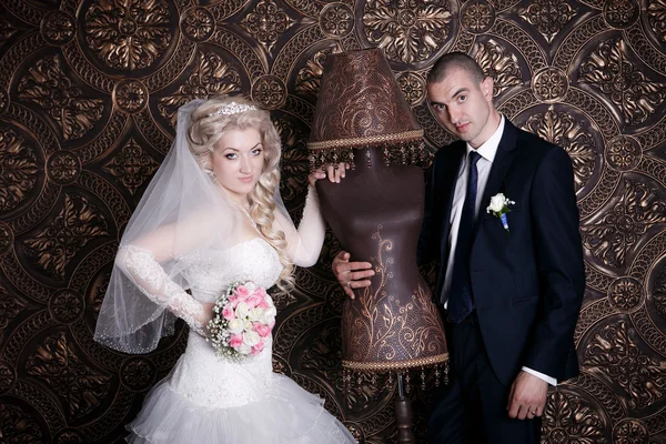 Glücklicher Bräutigam und die charmante Braut mit einem Rosenstrauß im Studio auf braunem Hintergrund — Stockfoto