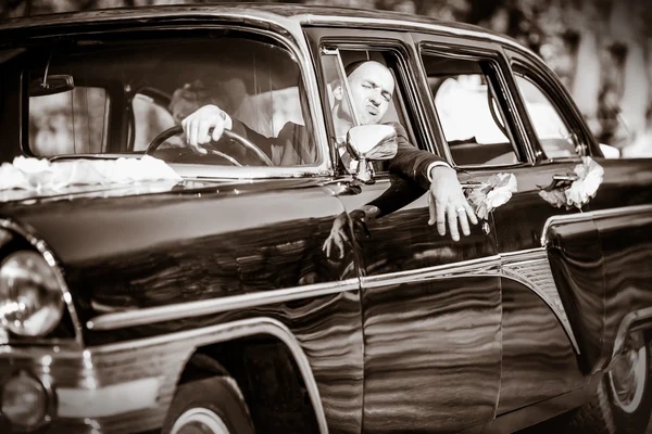 Alegre novio a la rueda de un negro viejo retro del coche — Foto de Stock