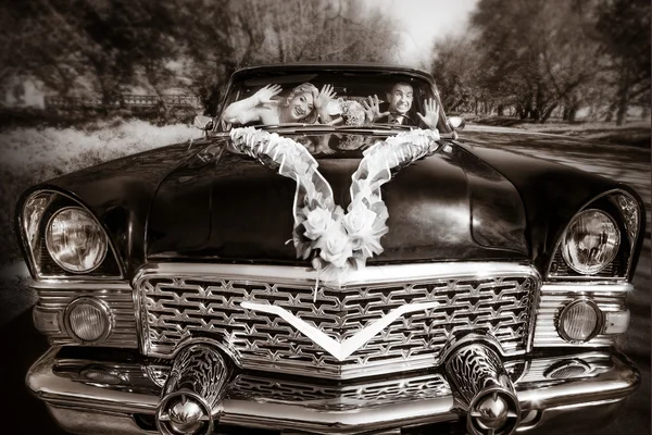 El novio alegre y la novia al volante negro viejo retro del coche — Foto de Stock