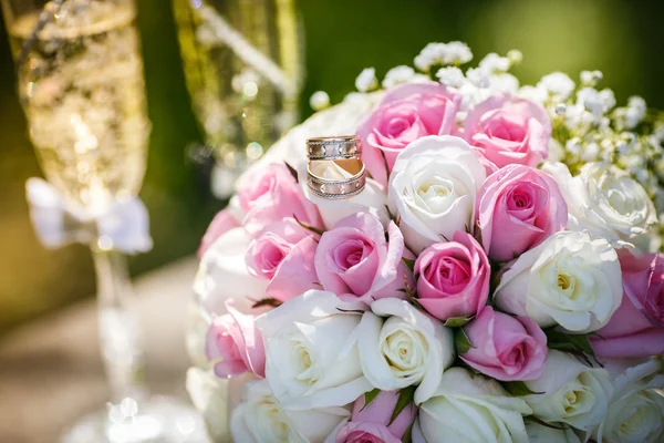 Huwelijksringen met rozen en glazen van champagne — Stockfoto