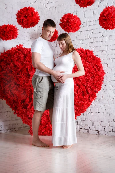 O marido e a esposa grávida no fundo do coração vermelho — Fotografia de Stock