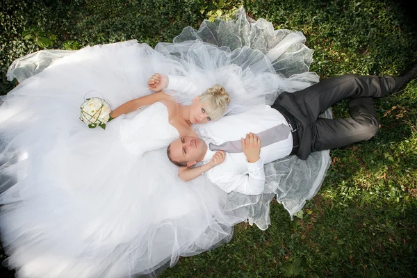 Happy bride and groom lying on green grass — Stock Photo, Image