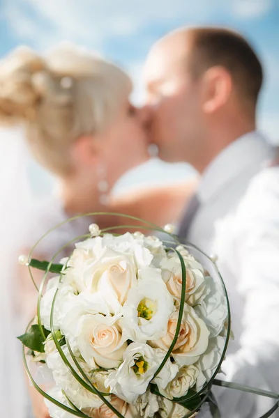 Gyönyörű csokor a menyasszony az esküvő pár csók a háttérben hajtja végre világos bézs-Rózsa — Stock Fotó