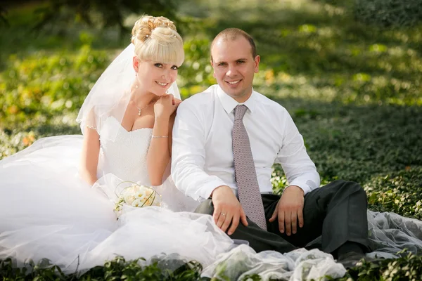 Bruden och brudgummen kramas och ser i ögonen på en annan sitter på ett grönt gräs — Stockfoto