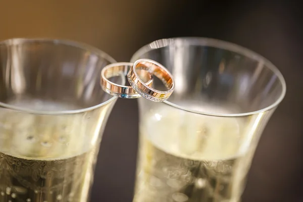 Wedding rings lie on champagne glasses — Stock Photo, Image