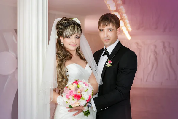 Groom and the bride with a wedding bouquet stand near a white column — Stock Photo, Image