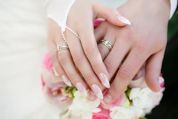 Handen van de bruidegom en de bruid met trouwringen en een bruiloft bouquet van rozen — Stockfoto