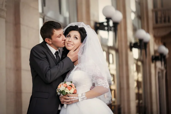 Novio y la novia con un puesto de ramo de bodas cerca de una columna blanca —  Fotos de Stock