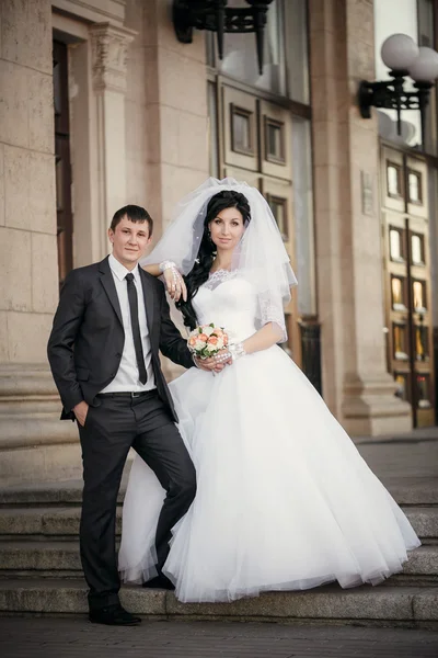 Bruidegom en de bruid met een bruiloft boeket staan in de buurt van een witte kolom — Stockfoto