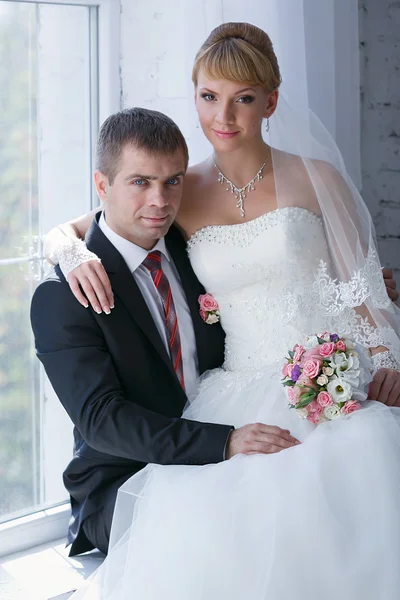 Lyckliga bruden och brudgummen på bröllopet promenad framför fönstret — Stockfoto