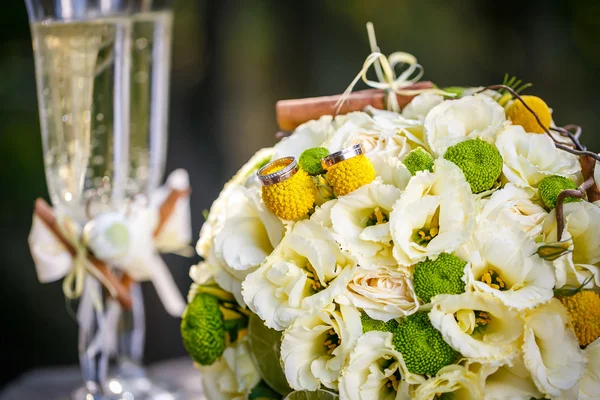 Anelli nuziali con mazzo nuziale da rose beige, cannella, un limone, una calce e occhiali di champagne — Foto Stock