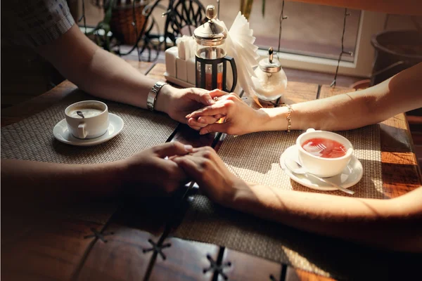 Las manos del chico y la mano de la chica en una mesa con una taza de té y una taza de café — Foto de Stock