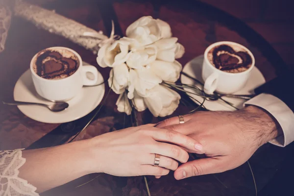 Duas xícaras de café e mão de noiva e noivo com anéis de casamento — Fotografia de Stock